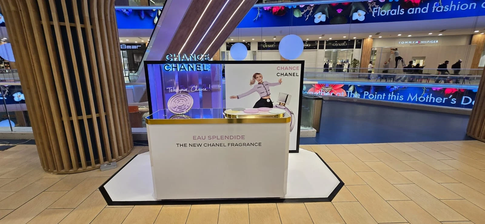 Branded fragrance promotion kiosk with a printed back panel and gold counter, set up in a shopping centre