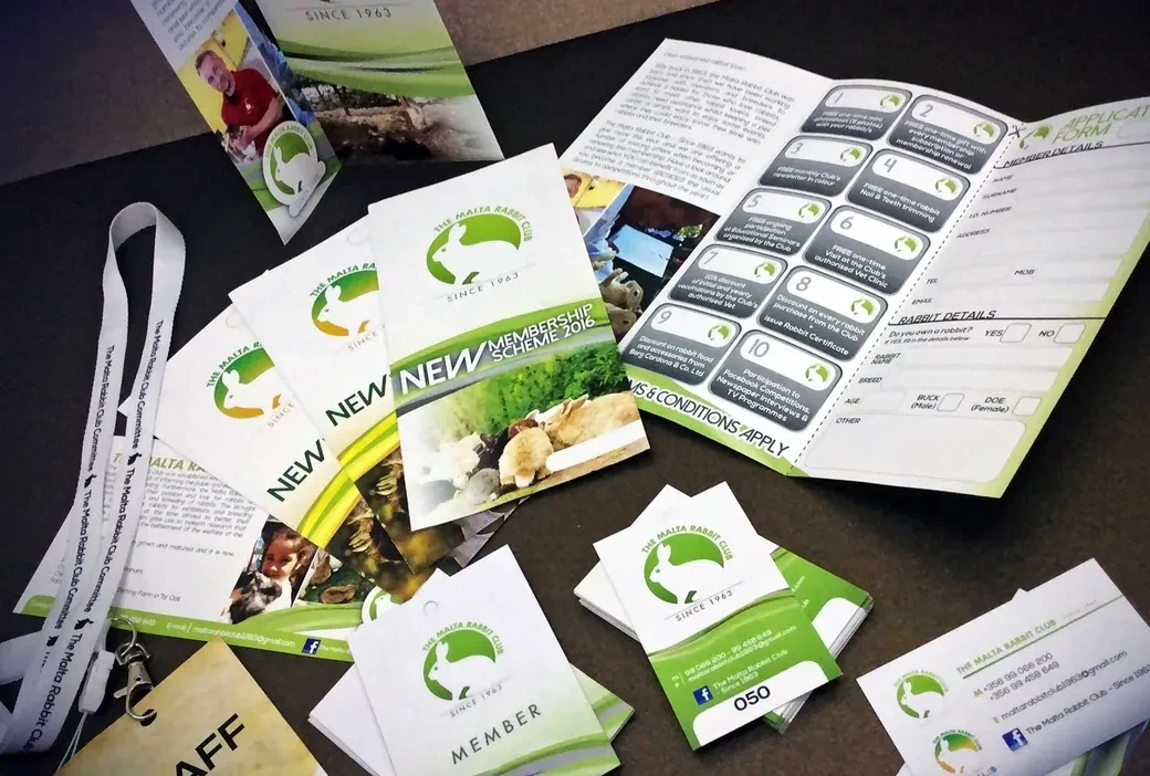 Printed brand identity set of folded leaflets, membership cards and a lanyard laid out on a dark table