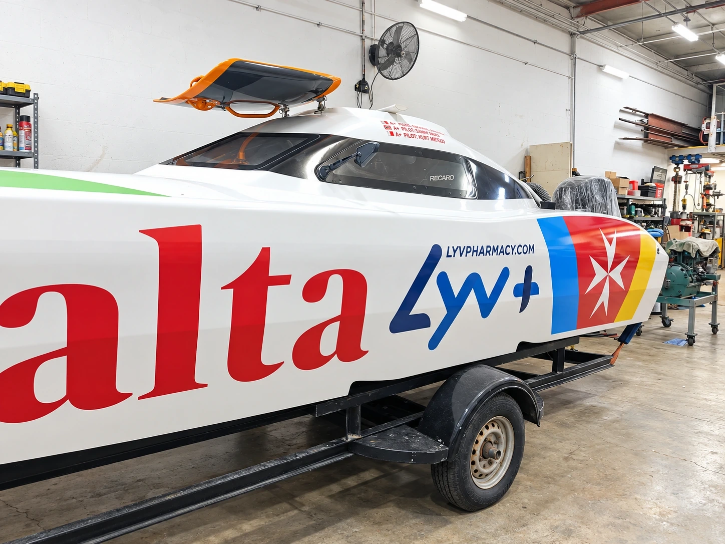 Racing powerboat wrapped in red, white and blue livery, standing on its trailer in a workshop