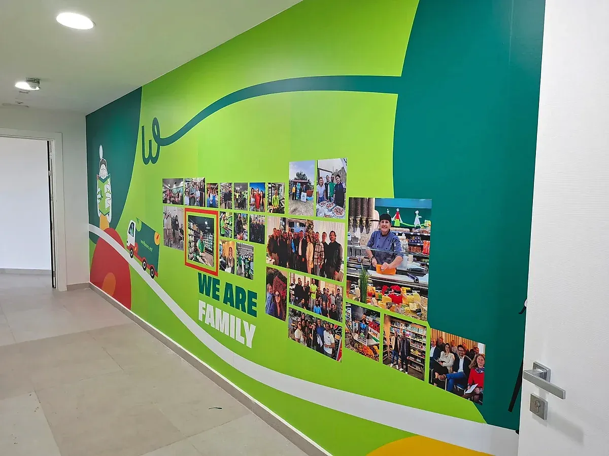 Green corridor wall graphic combining flowing brand shapes with a printed photo collage