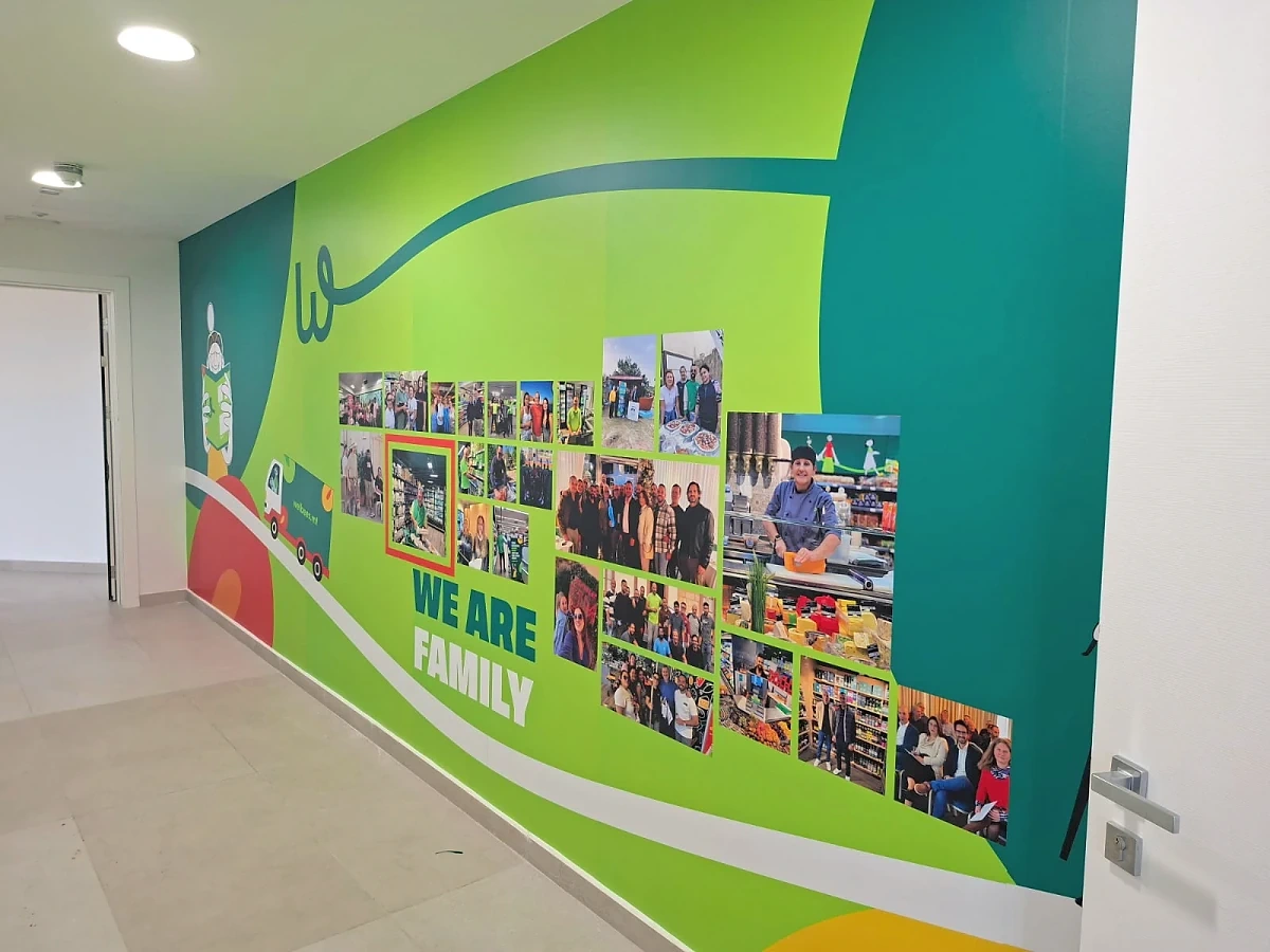Green corridor wall graphic combining flowing brand shapes with a printed photo collage