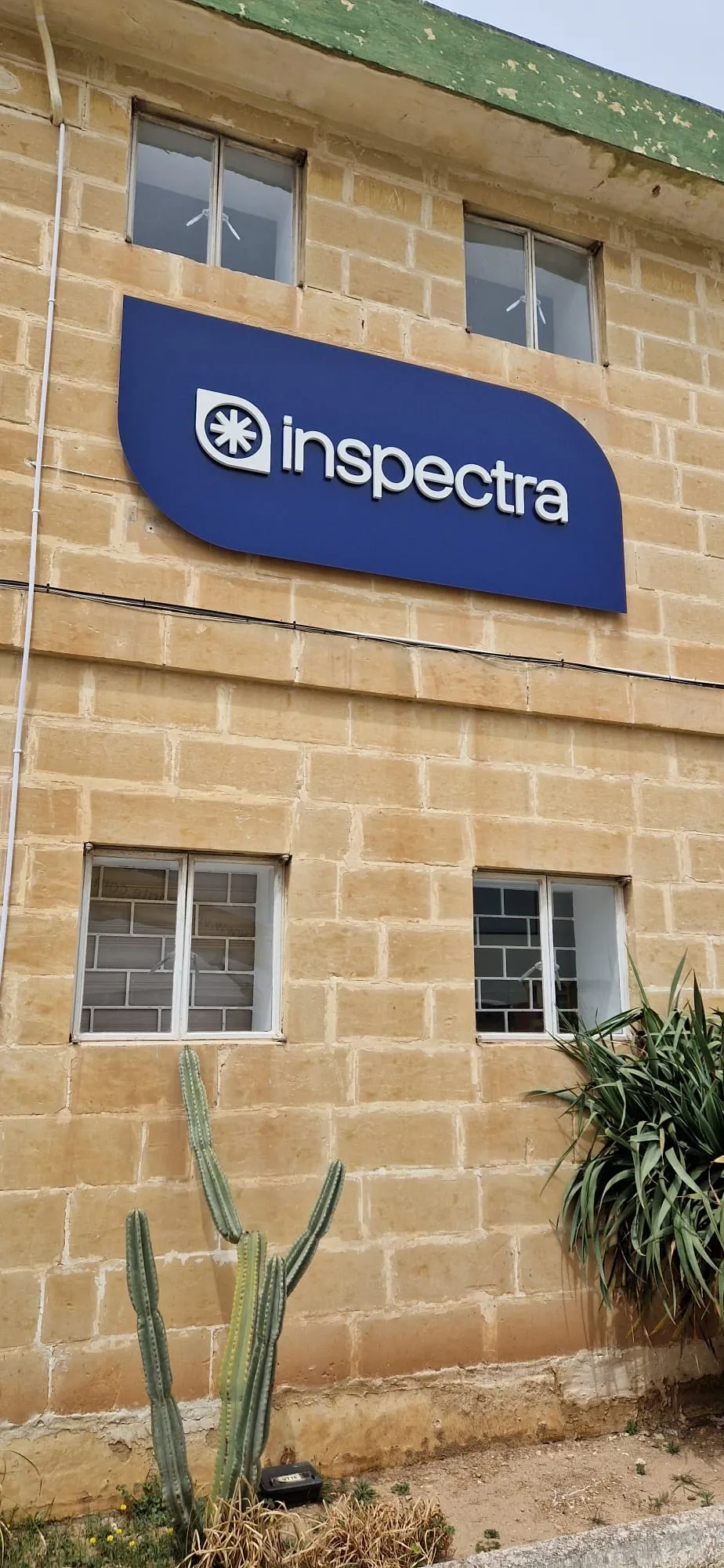 Blue shaped fascia sign mounted high on a limestone building above two windows
