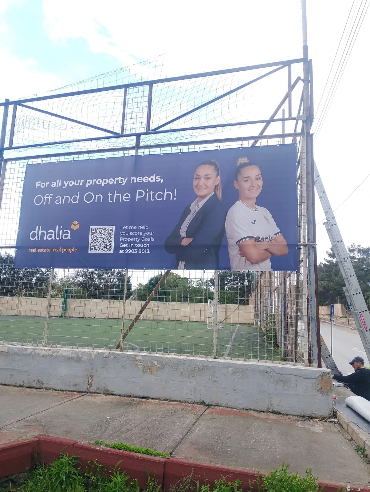Printed banner tensioned onto the fence of a floodlit sports pitch