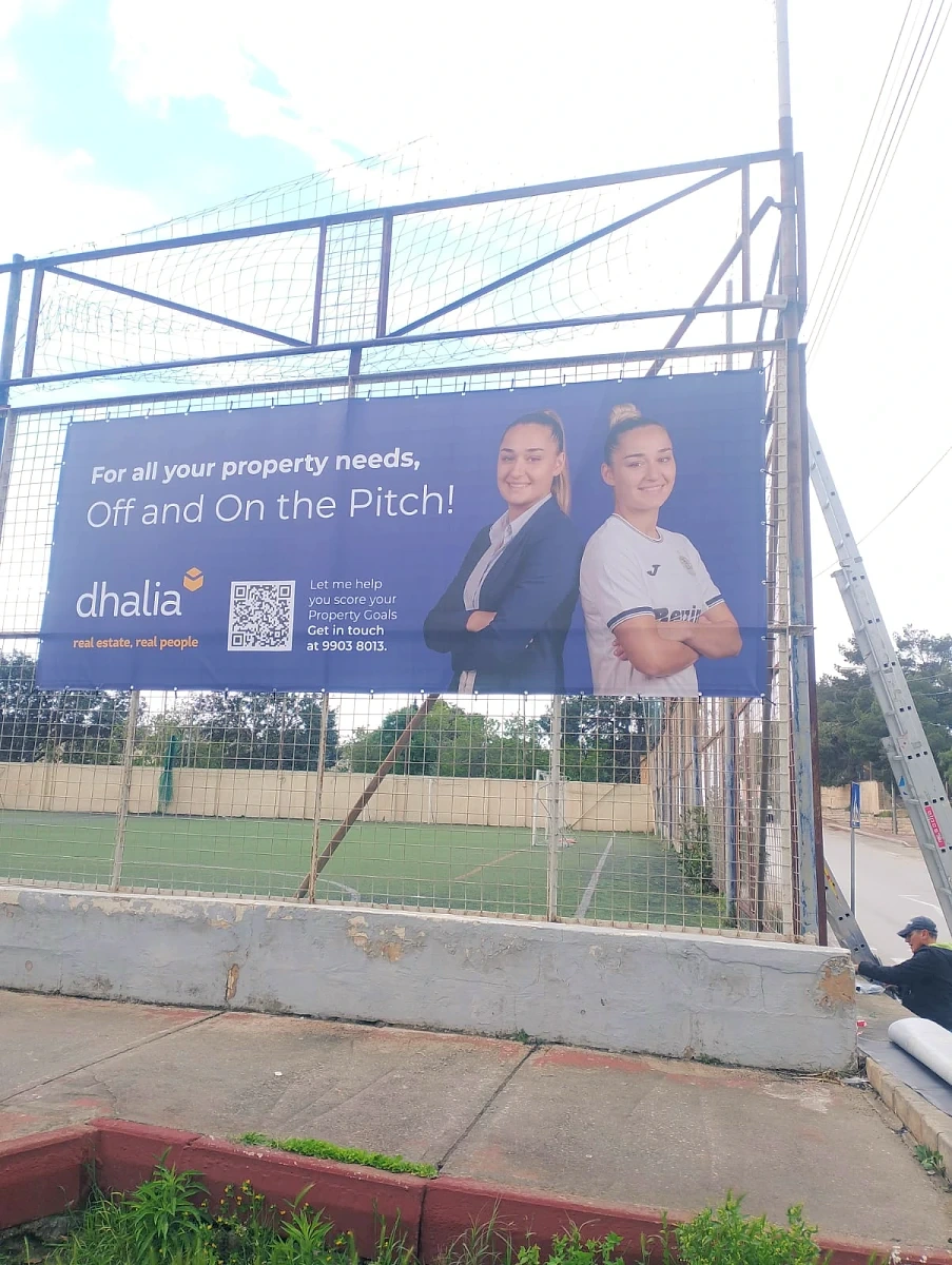 Printed banner tensioned onto the fence of a floodlit sports pitch