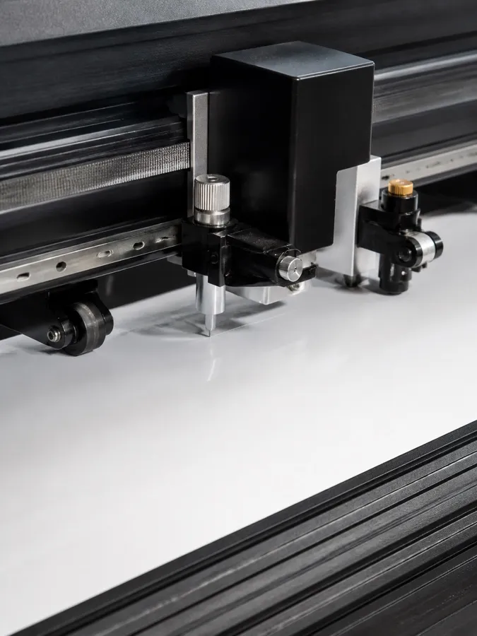 Close view of a cutting plotter blade tracking across plain white vinyl