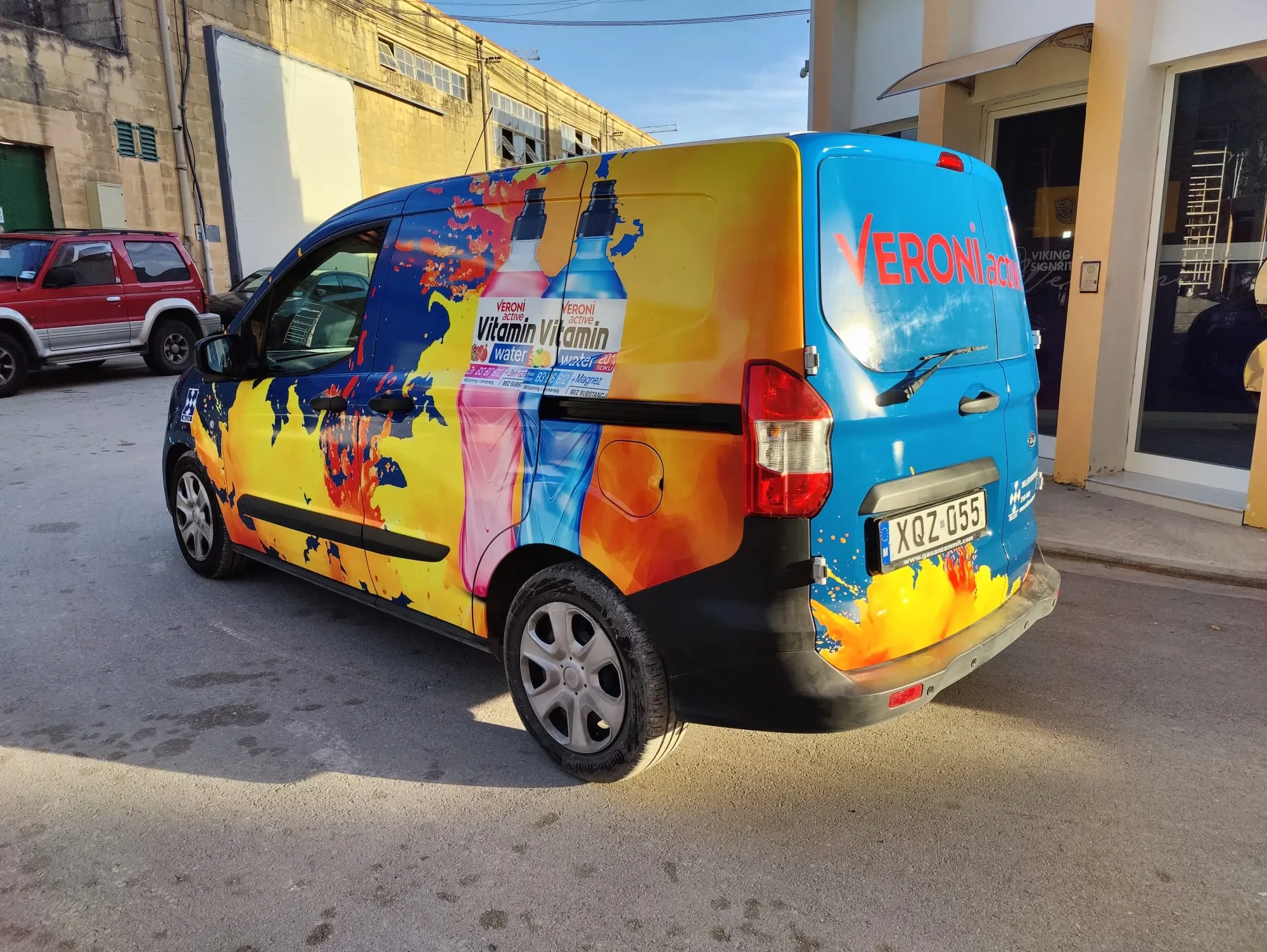 Compact van wrapped in a bright orange and blue pattern with printed drink bottles