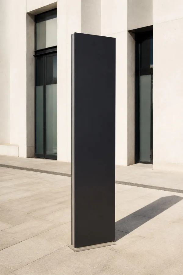Blank black wayfinding totem casting a long morning shadow in a stone plaza