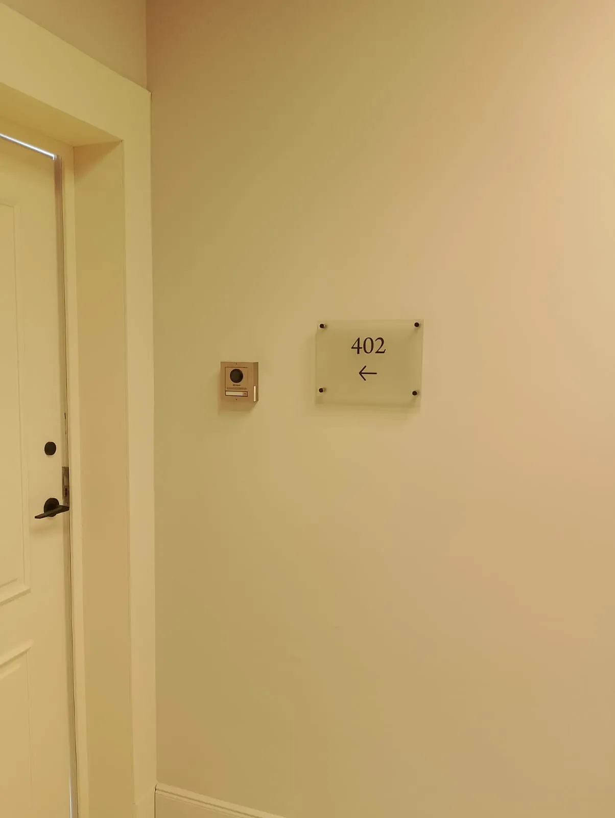 Small acrylic room number plate with an arrow, fixed to a corridor wall on standoffs