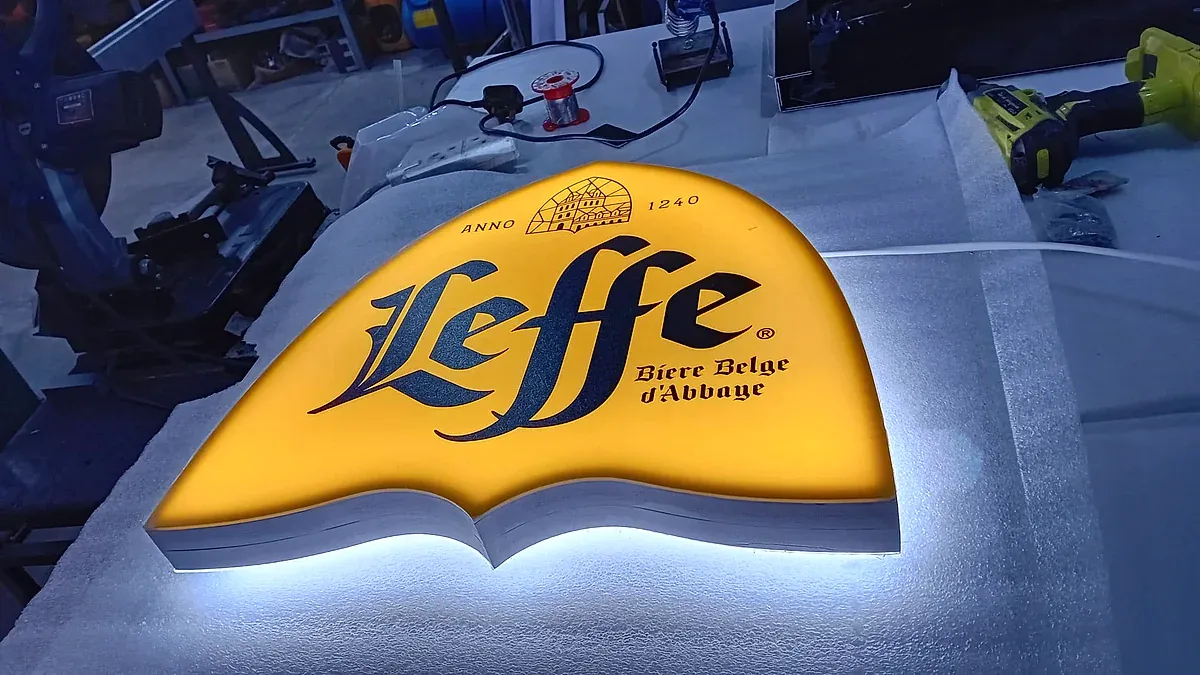 Shaped halo-lit sign lying face up on a workshop bench, its yellow face glowing against the light behind it