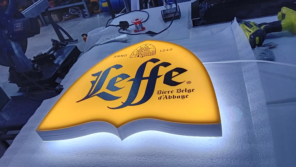 Shaped halo-lit sign lying face up on a workshop bench, its yellow face glowing against the light behind it