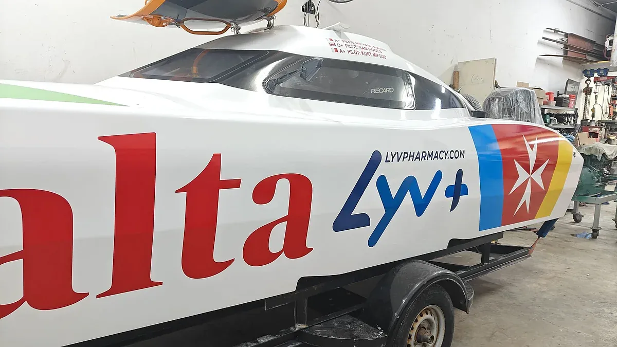 Racing powerboat wrapped in red, white and blue livery, standing on its trailer in a workshop