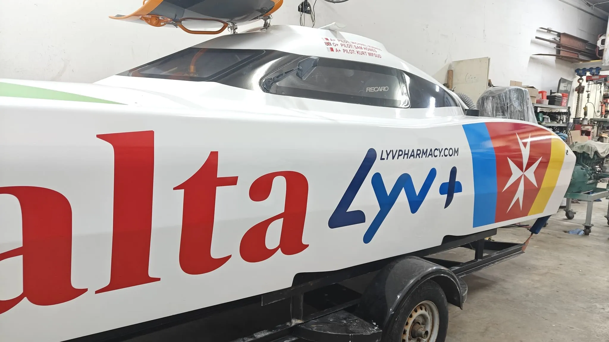 Racing powerboat wrapped in red, white and blue livery, standing on its trailer in a workshop