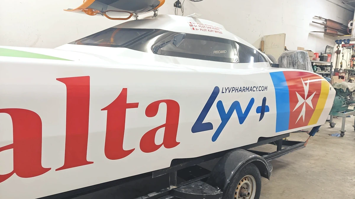 Racing powerboat wrapped in red, white and blue livery, standing on its trailer in a workshop