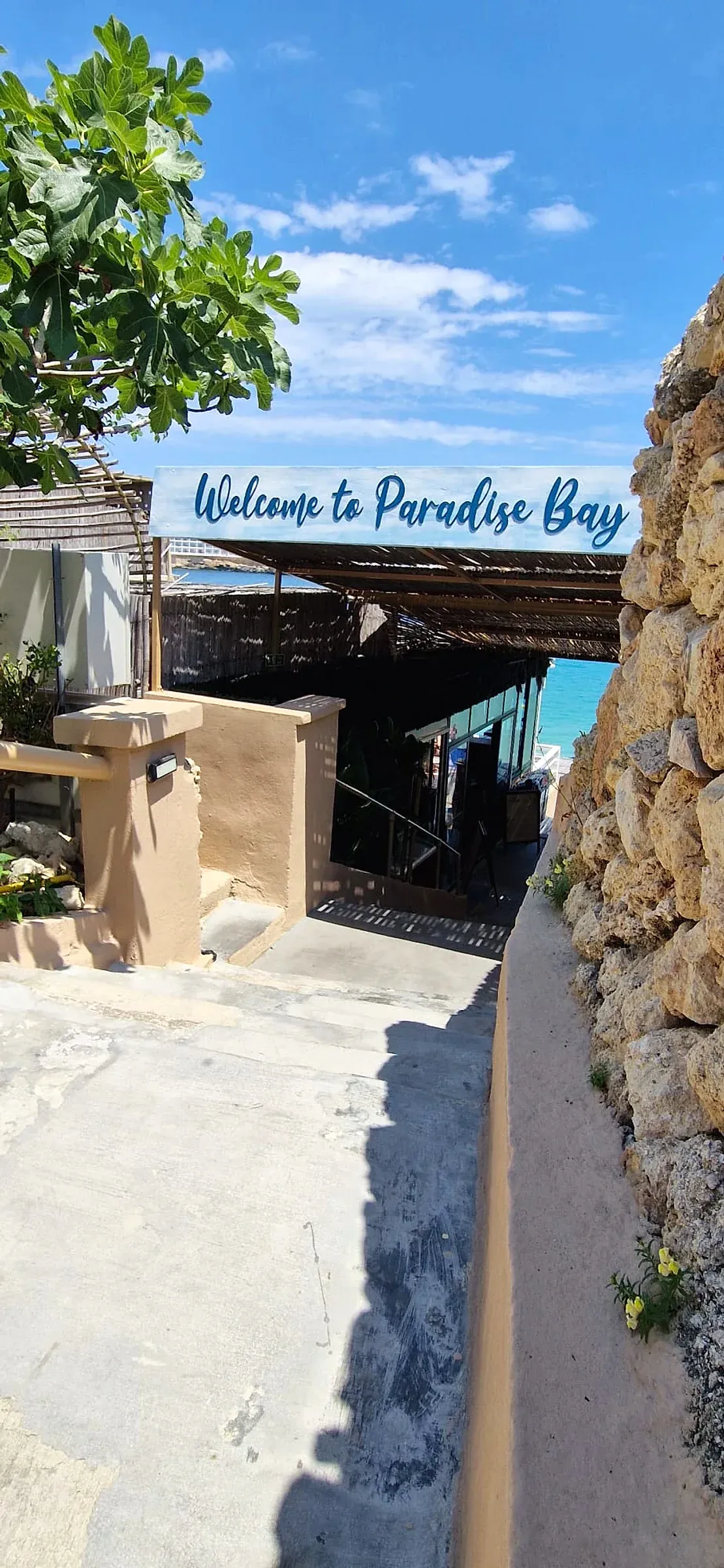 Hand-lettered welcome sign mounted above a shaded walkway leading down to a bay