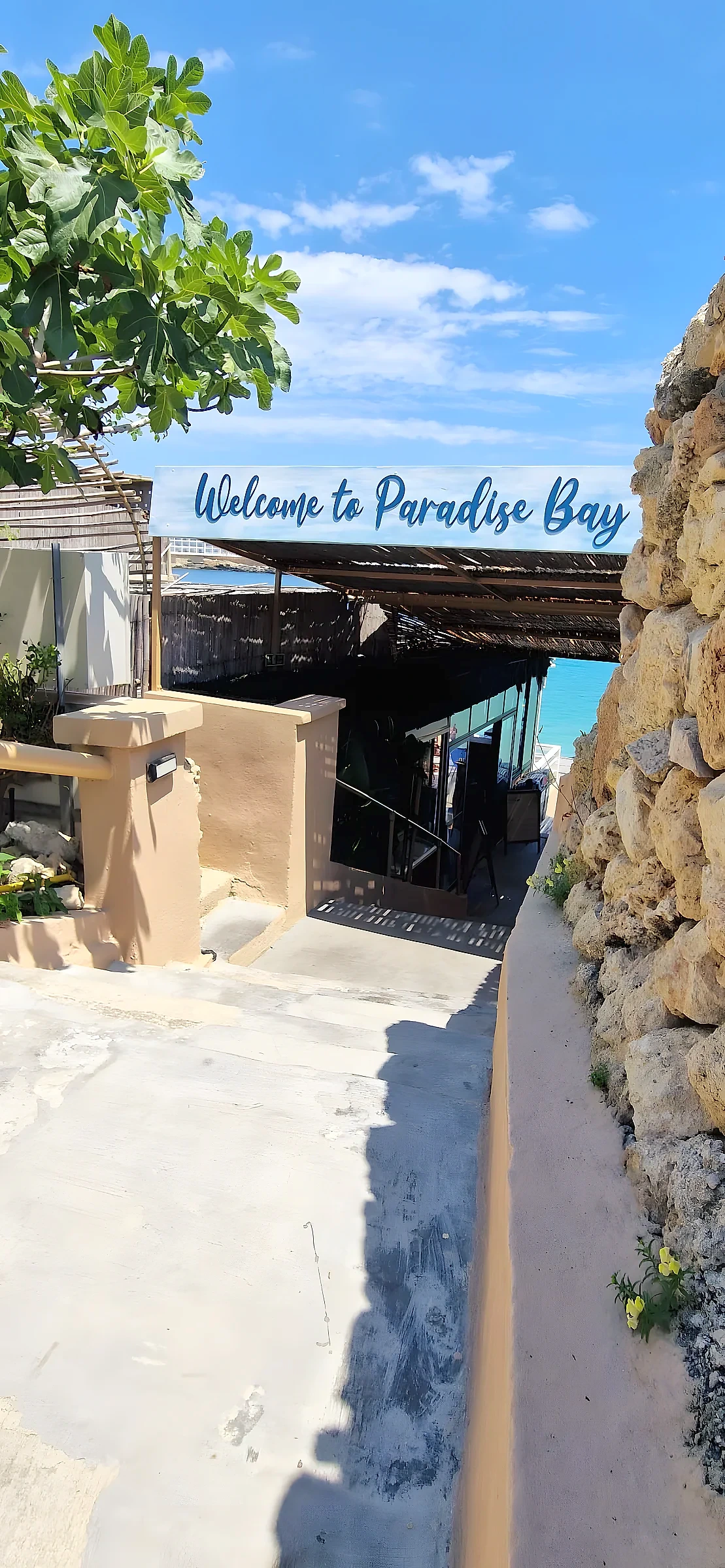 Hand-lettered welcome sign mounted above a shaded walkway leading down to a bay