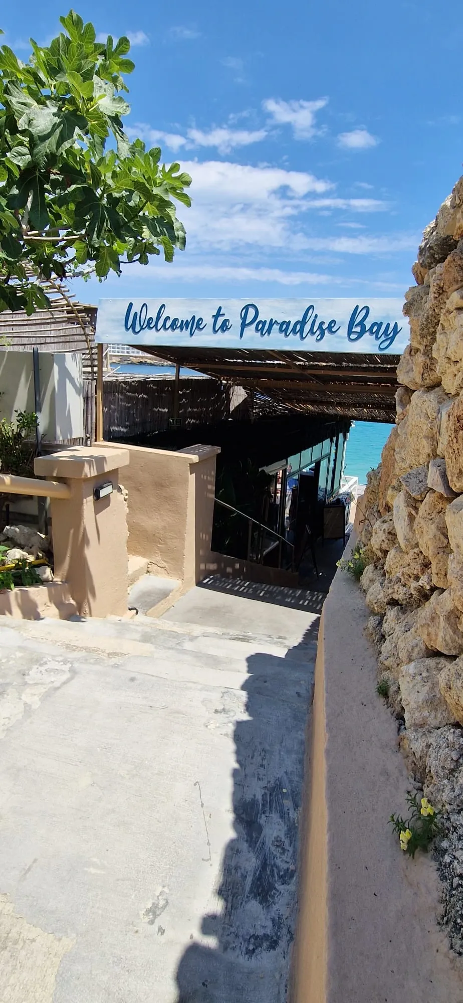 Hand-lettered welcome sign mounted above a shaded walkway leading down to a bay