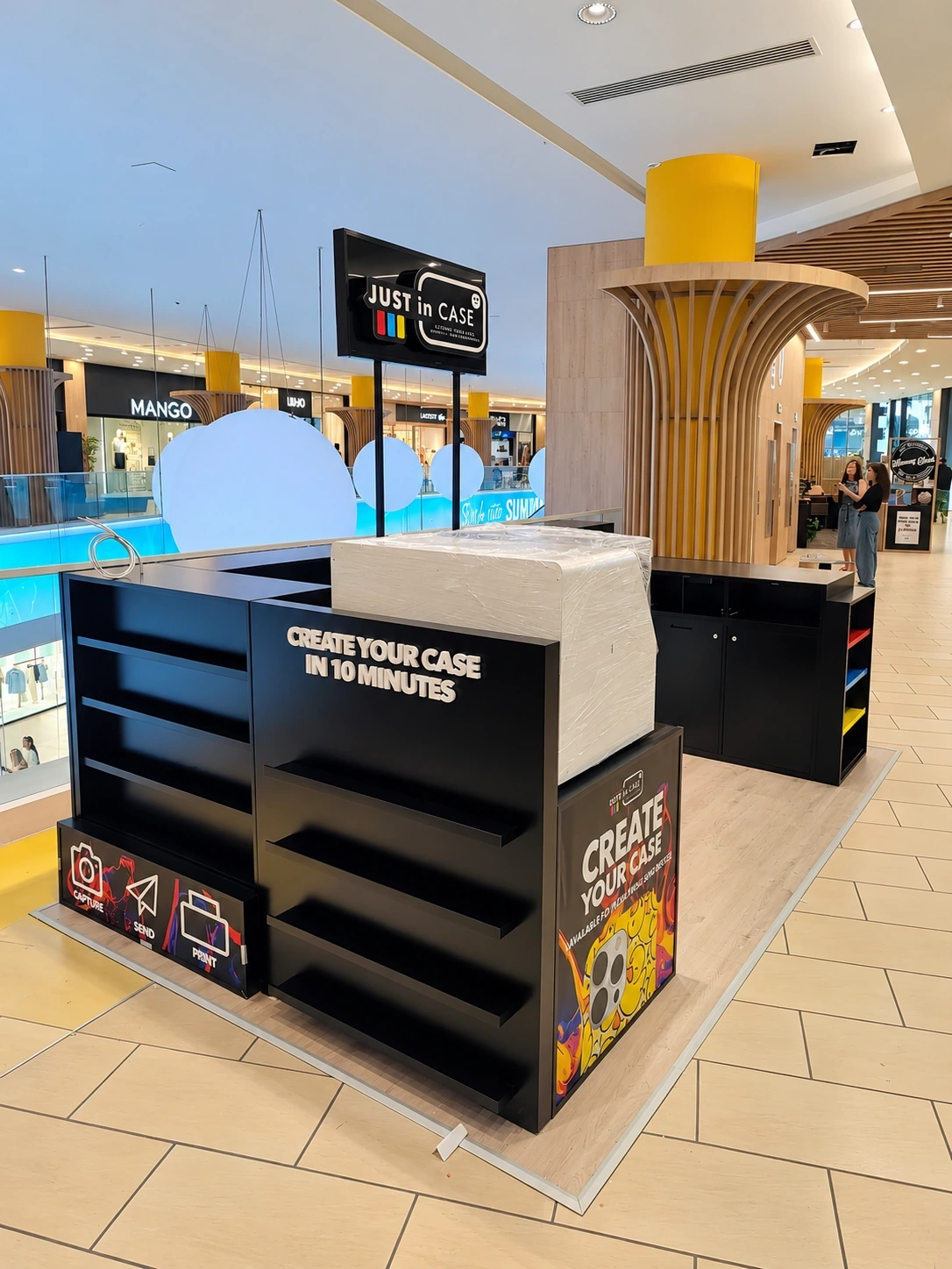 Black phone-case kiosk with printed panels and a hanging header sign in a shopping centre