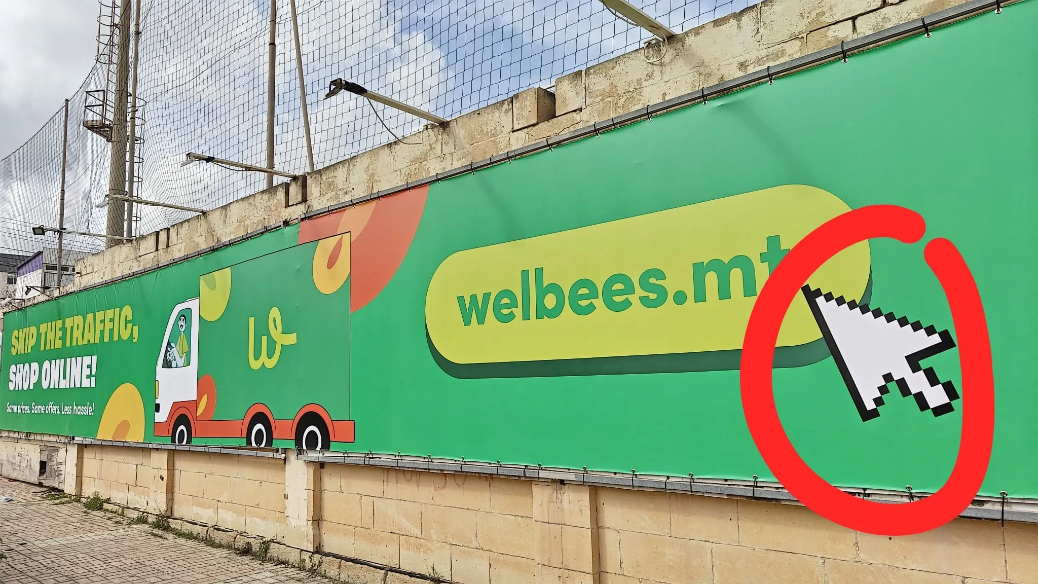 Long printed hoarding banner tensioned along a wall, showing a delivery van illustration and a web address