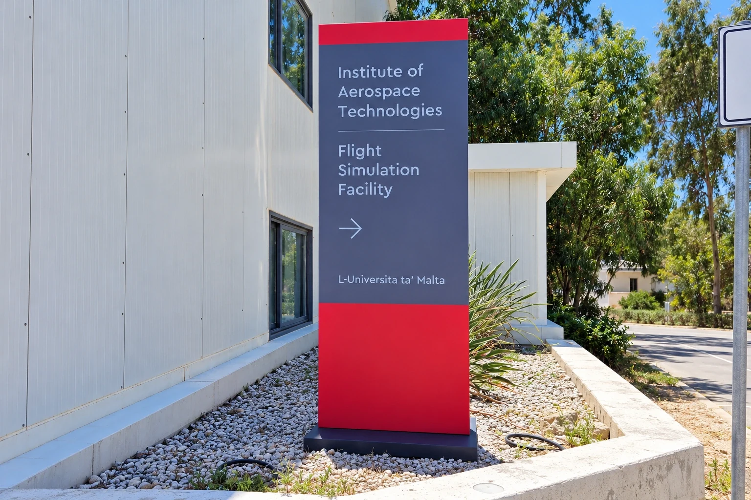 Red and grey free-standing totem sign pointing visitors to a flight simulation facility outside a modern building