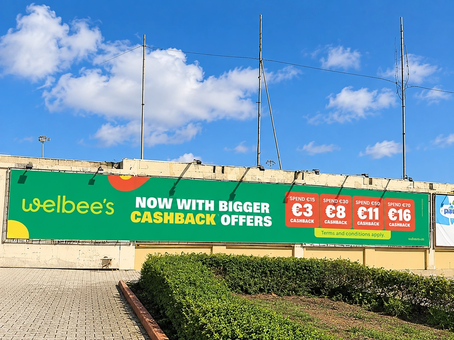 Long green promotional banner with cashback offers fixed along a fence beside a sports ground