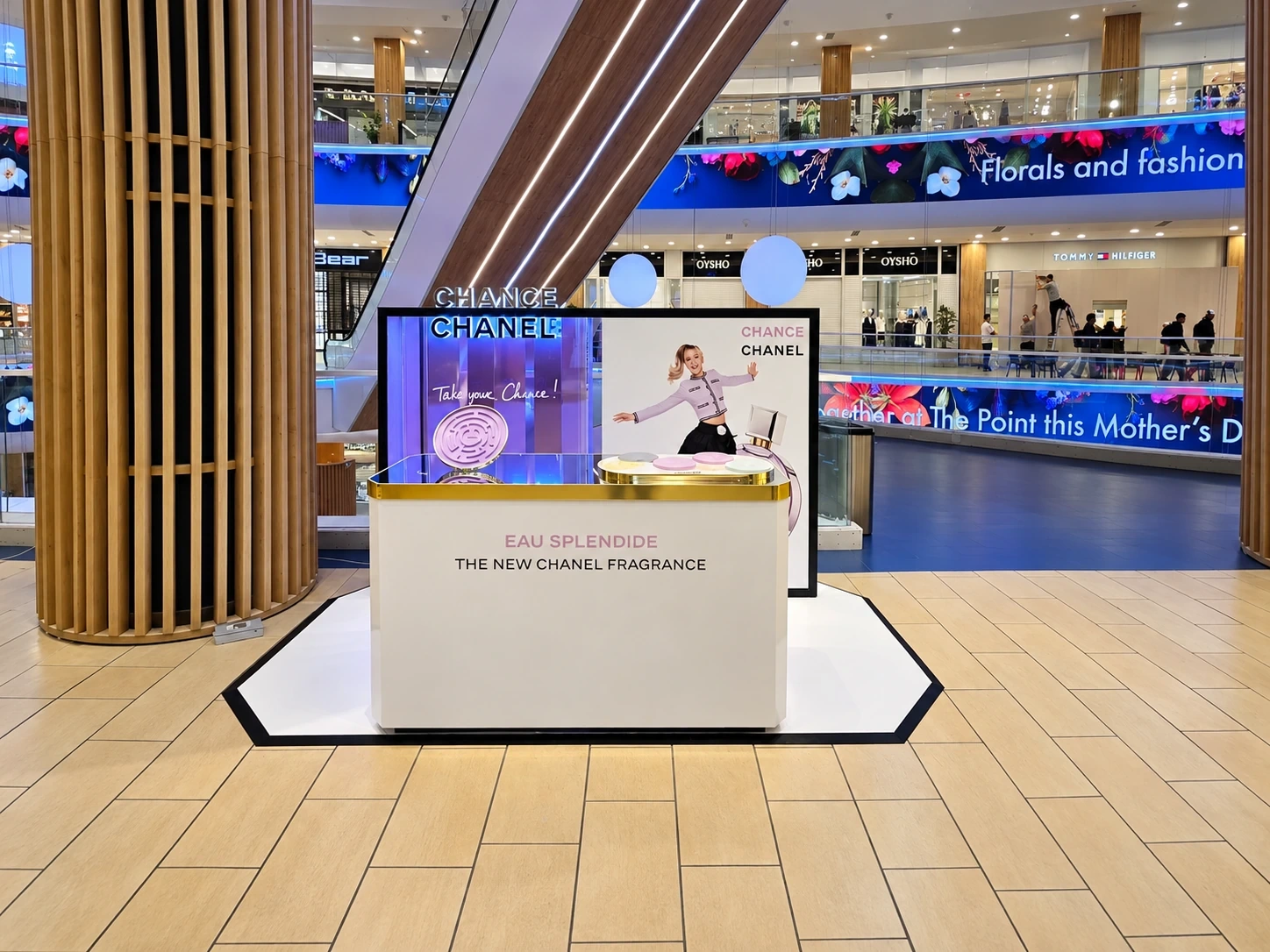Branded fragrance promotion kiosk with a printed back panel and gold counter, set up in a shopping centre