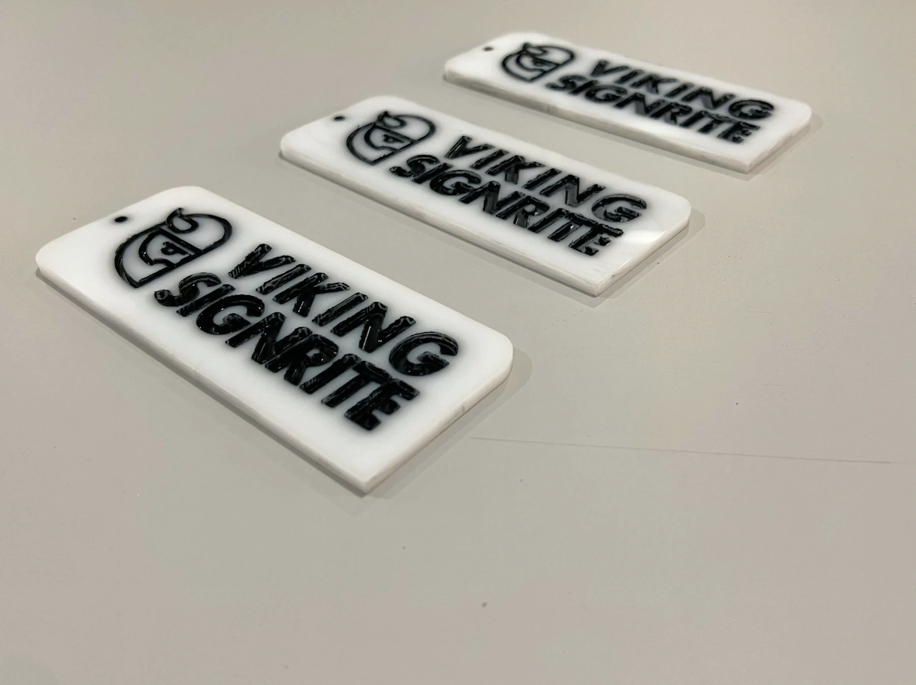 Three engraved white acrylic tags carrying the Viking Signrite logo, laid out in a diagonal row on a pale surface