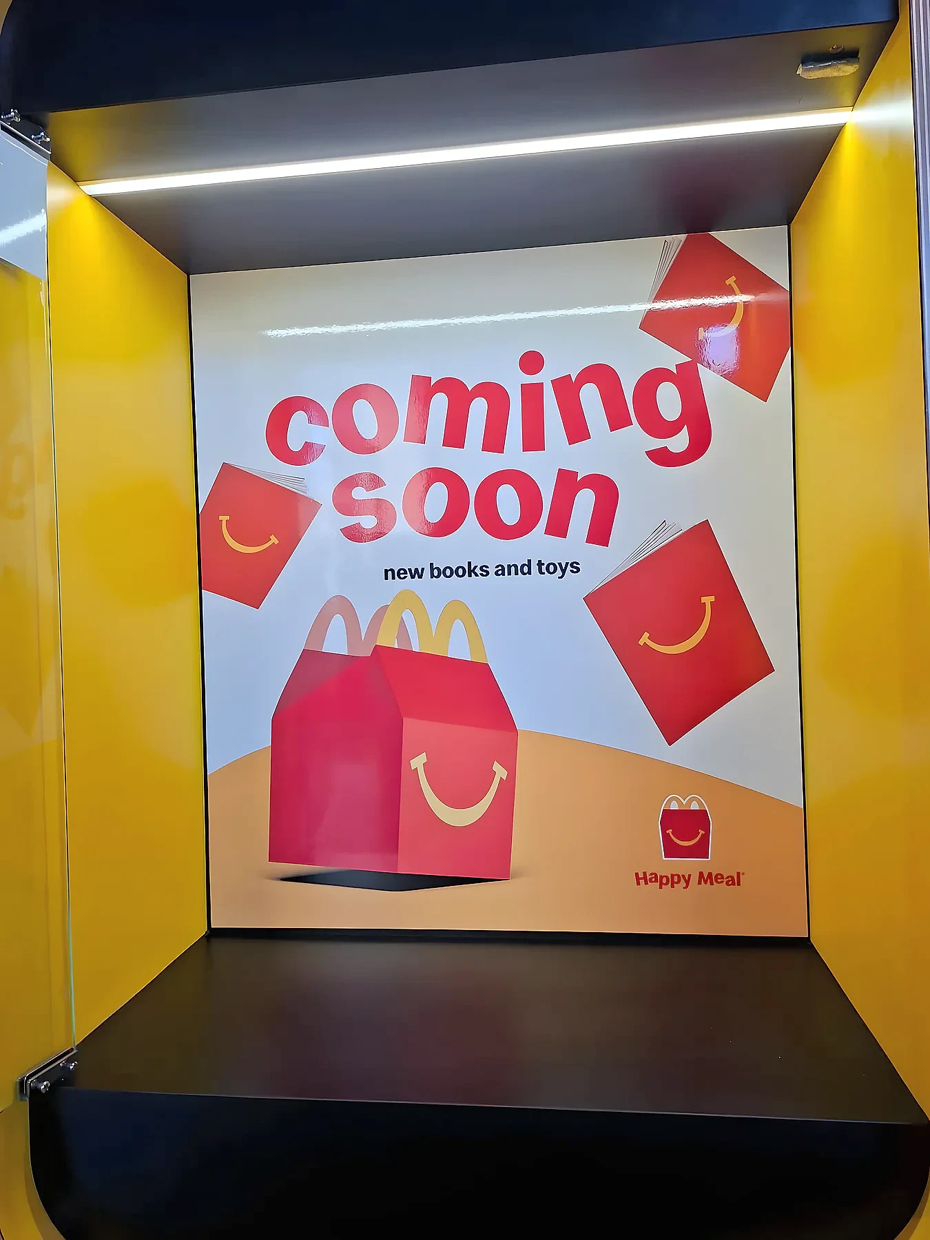 Illuminated display cabinet holding a printed coming soon panel for new children's meal books and toys