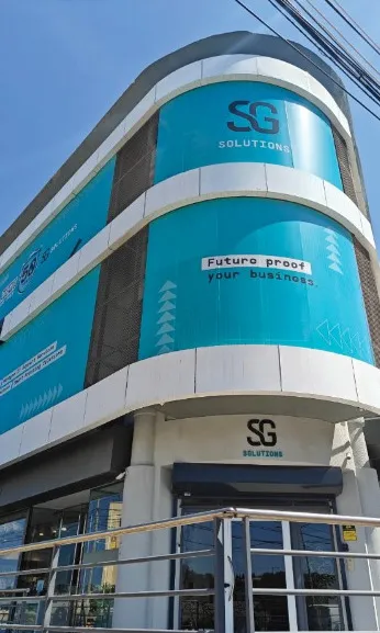 Curved multi-storey building facade wrapped in printed signage panels, with an illuminated sign above the entrance