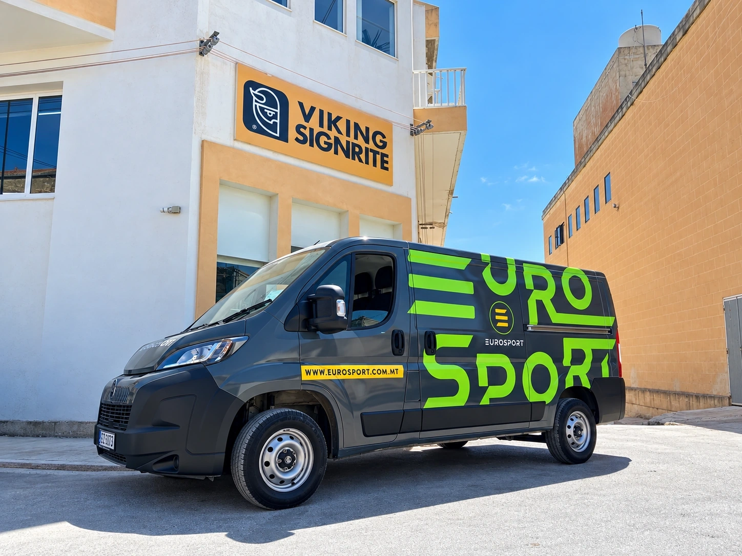 Grey panel van in a large green sports-brand livery, parked outside a building carrying a Viking Signrite sign