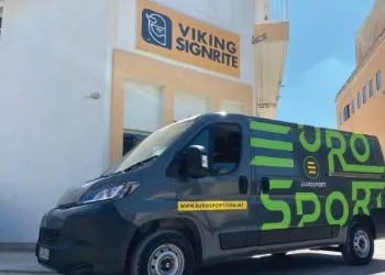 Dark grey delivery van wrapped in bold green vehicle graphics, parked outside a signage workshop
