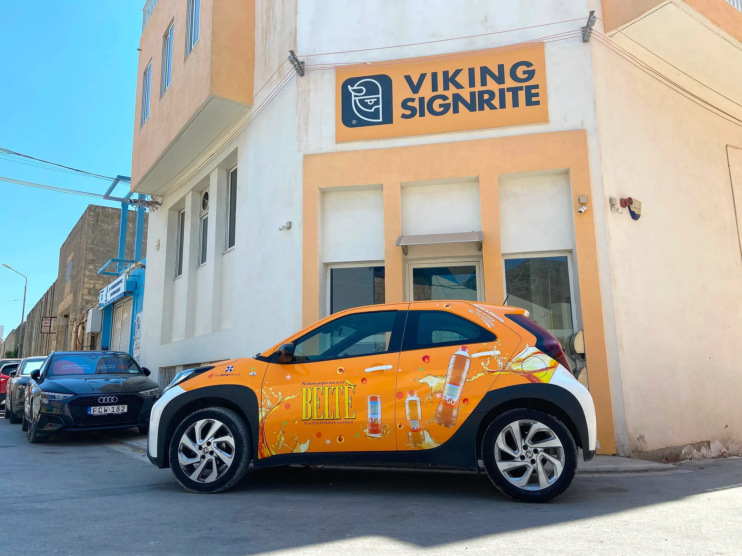 Compact car wrapped in an orange printed drinks design, parked in the sun outside the Viking Signrite workshop