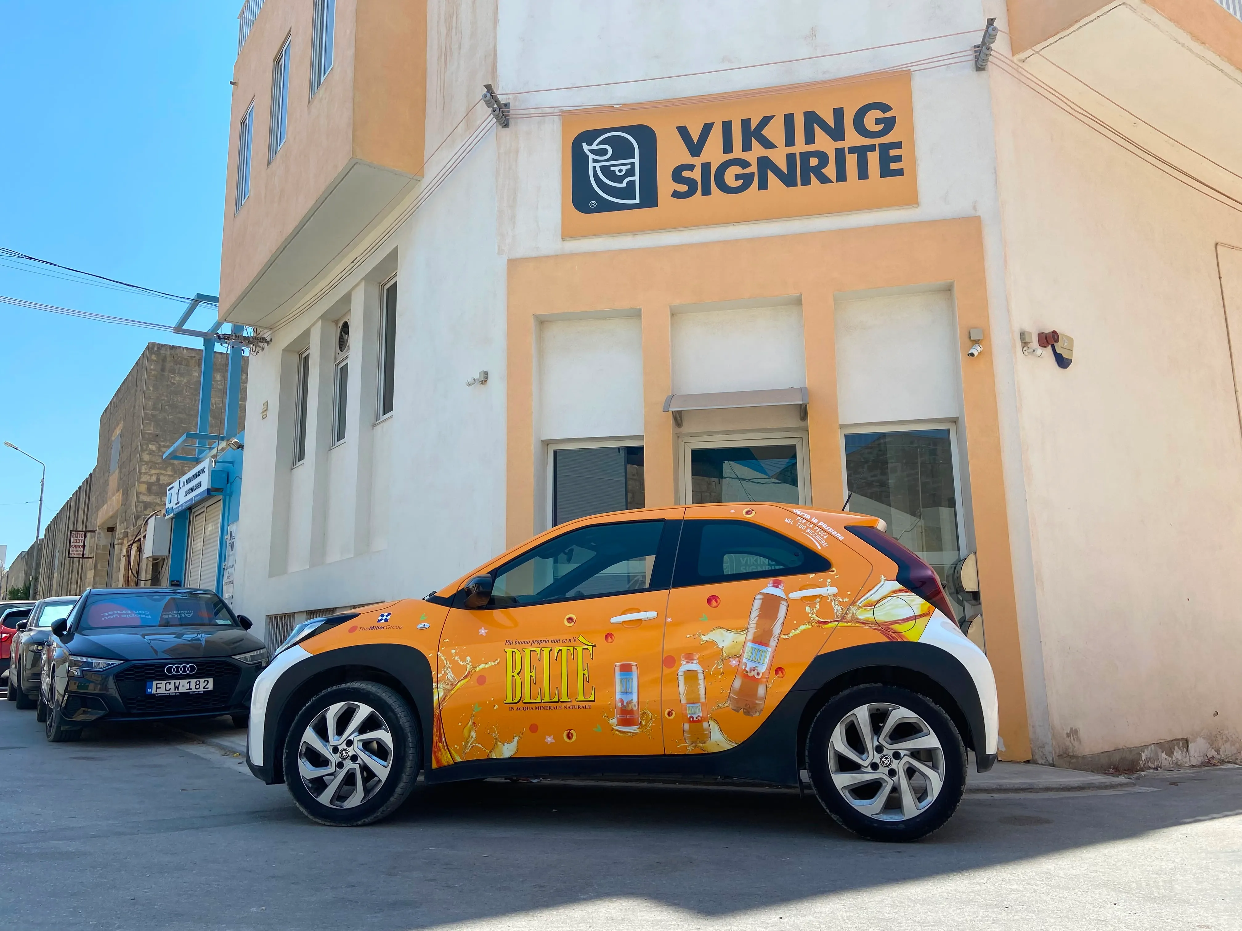 Compact car wrapped in an orange printed drinks design, parked in the sun outside the Viking Signrite workshop