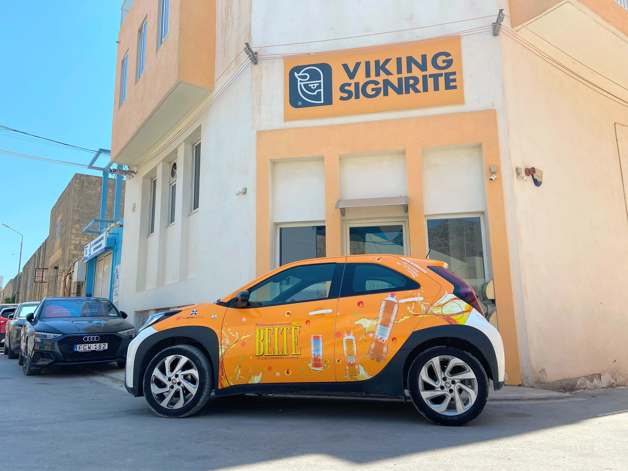 Compact car wrapped in an orange printed drinks design, parked in the sun outside the Viking Signrite workshop