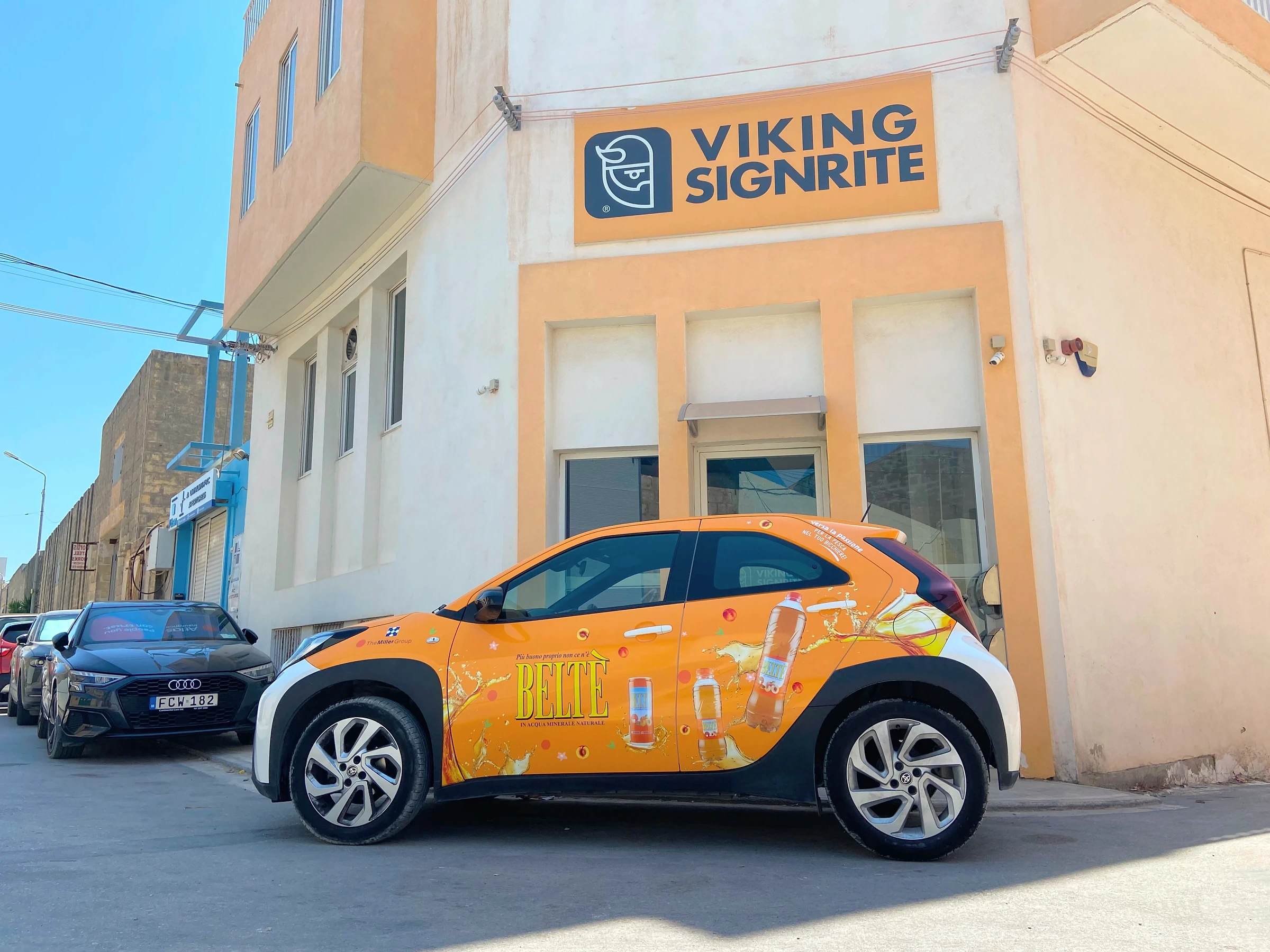 Compact car wrapped in an orange printed drinks design, parked in the sun outside the Viking Signrite workshop