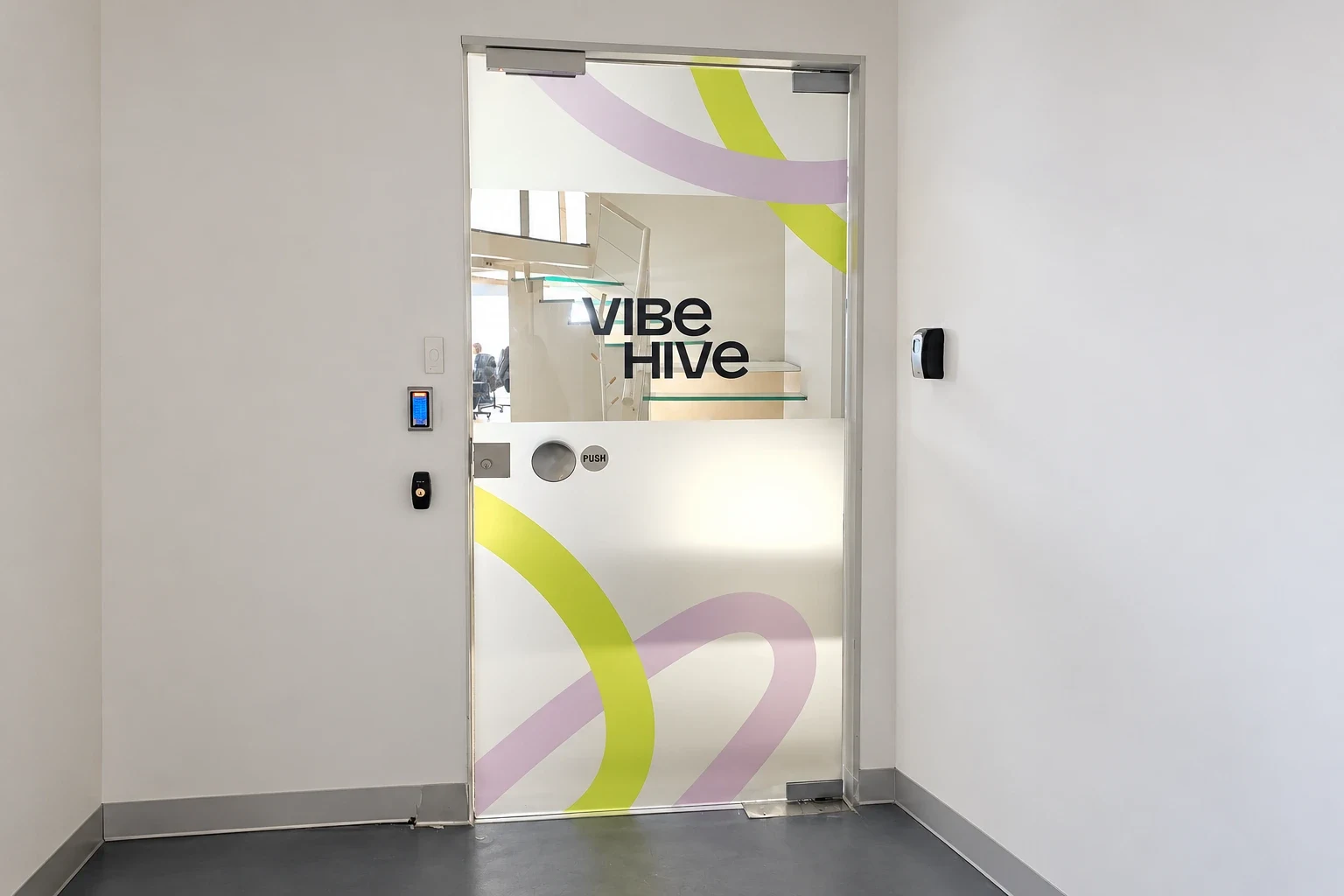 Glass door with frosted film printed in yellow and pink curves, the company name readable through a clear band