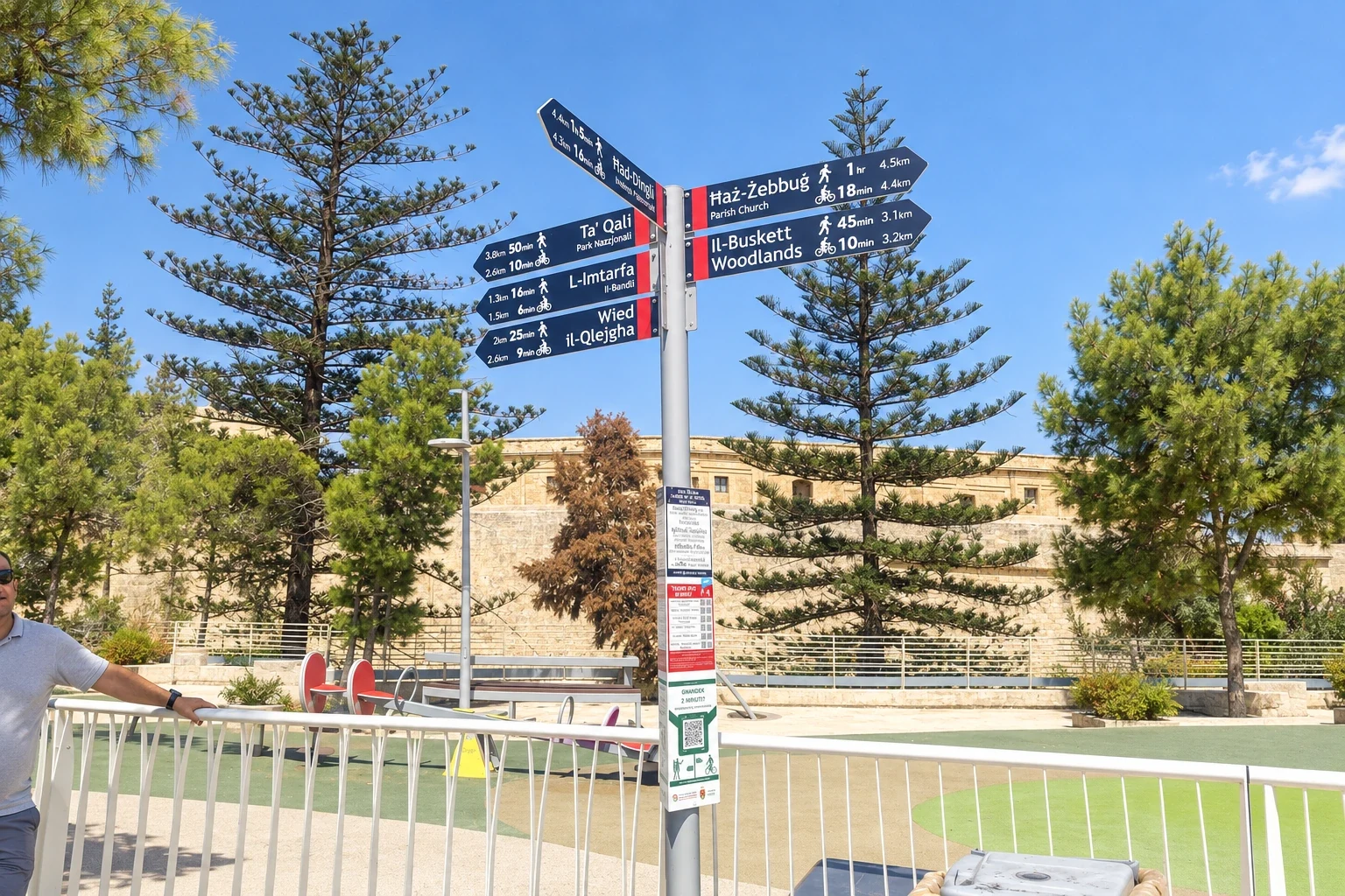 Fingerpost with eight destination arms on a tall post against pine trees and a bastion wall