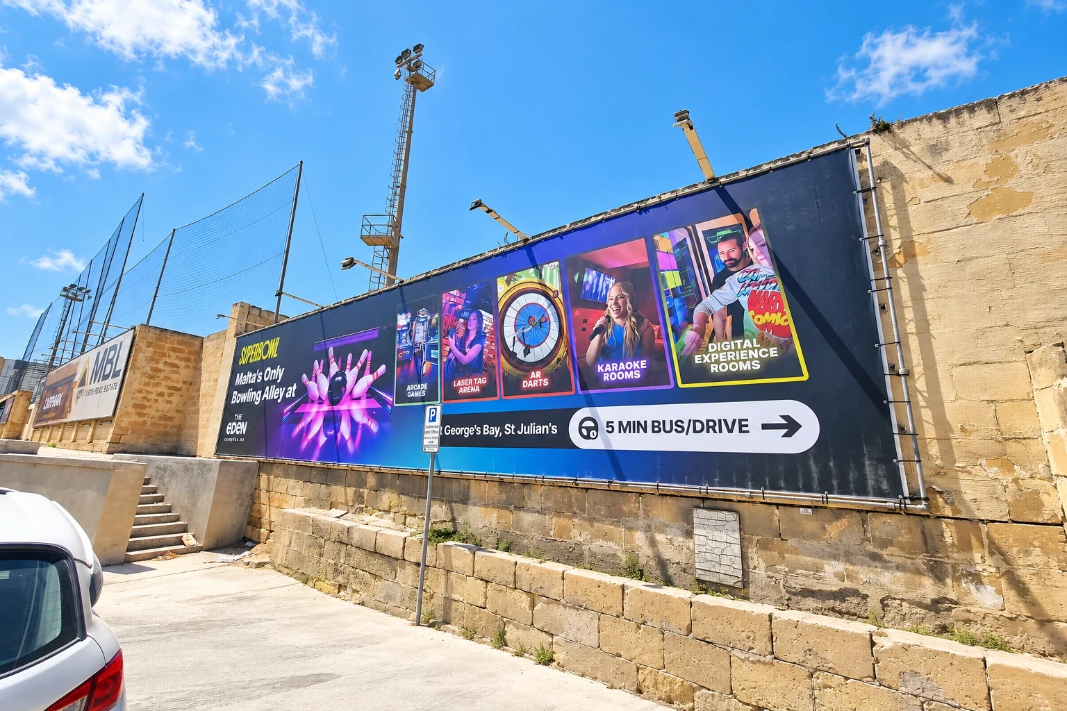 Wide dark banner with photographic panels for bowling, darts and karaoke rooms fixed along a stone site hoarding