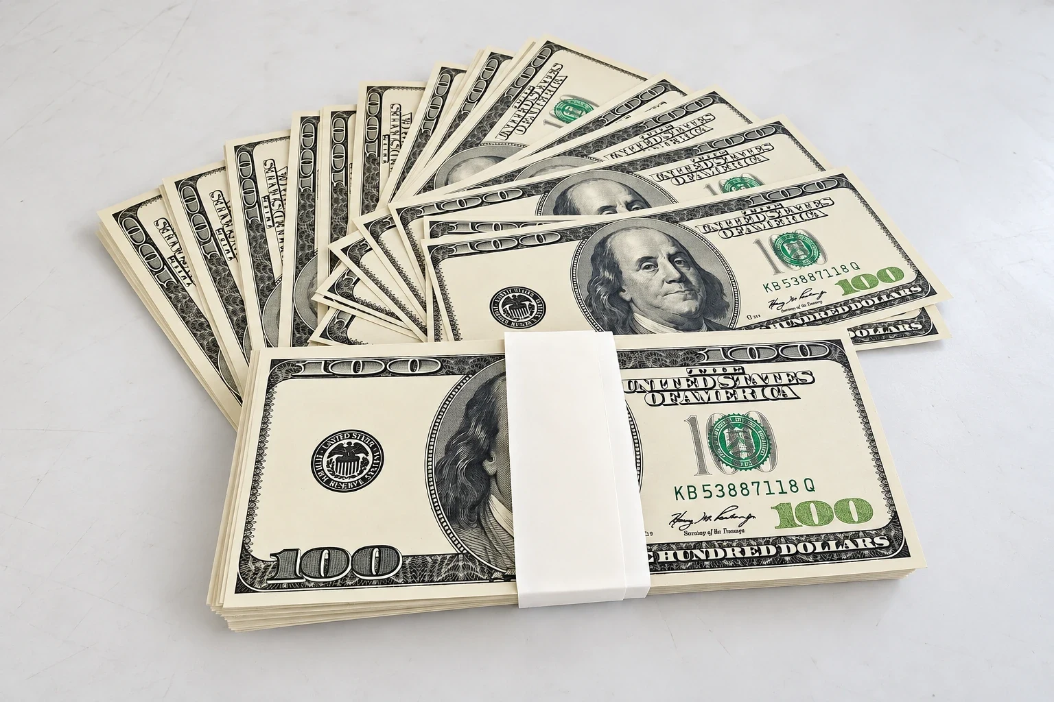 Fanned stacks of printed prop hundred dollar film notes banded together on a white surface