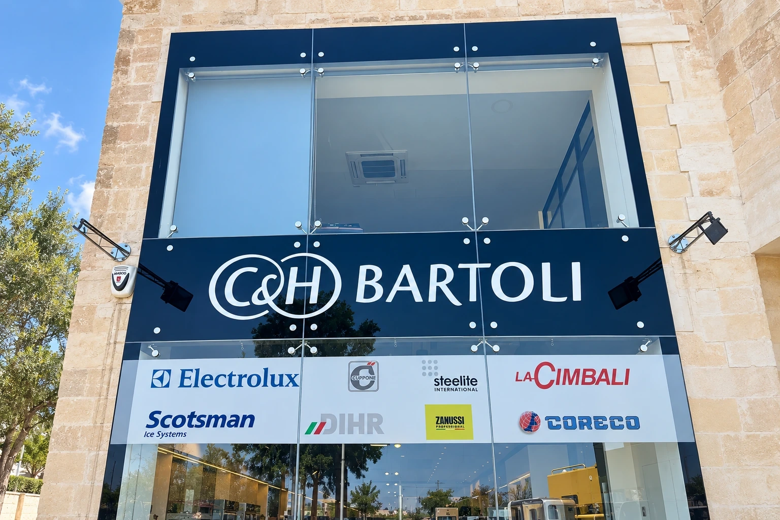 Dark fascia sign with large built-up lettering above a row of supplier plates on a glazed building frontage