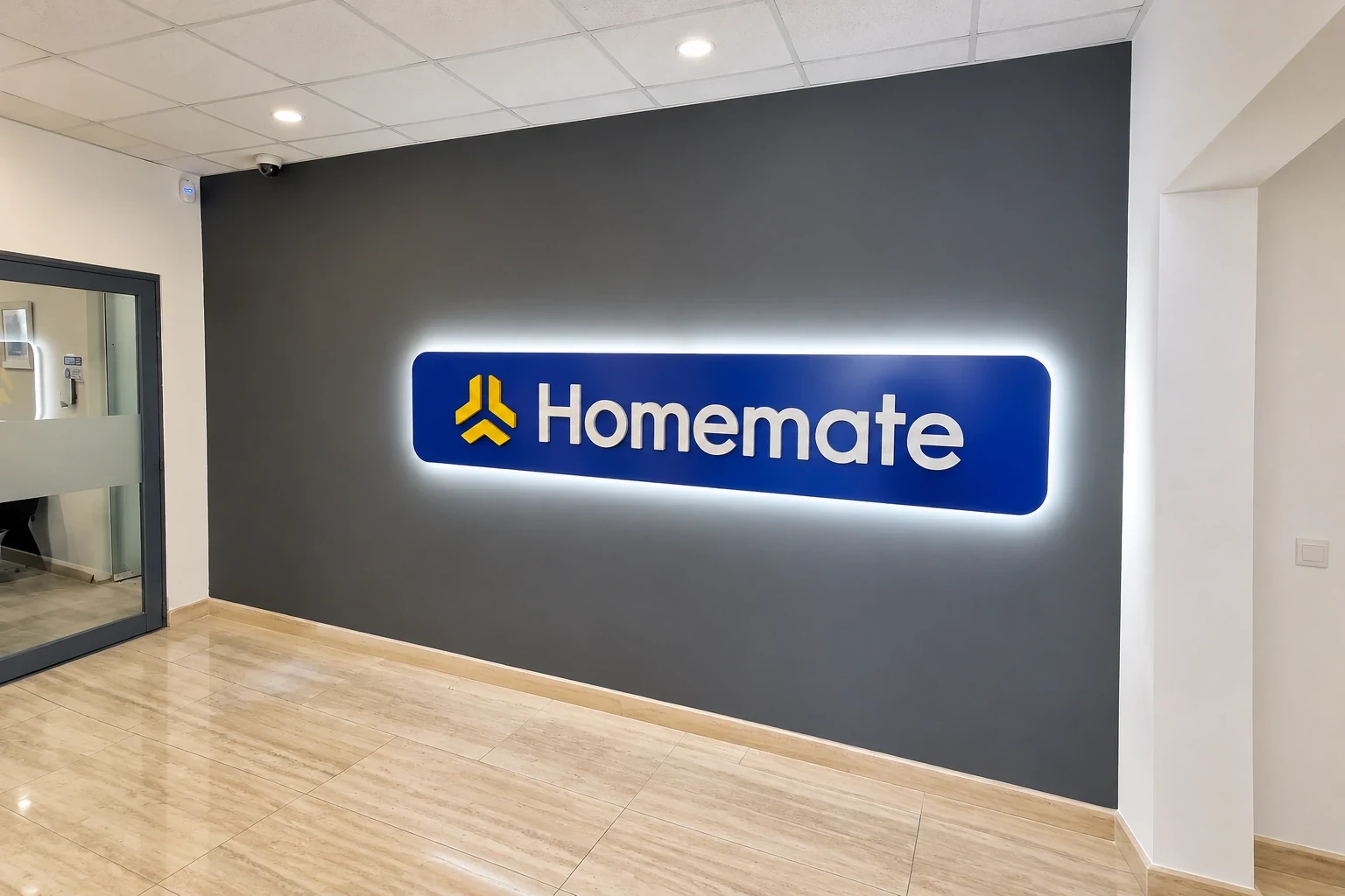 Blue halo-lit logo panel glowing against a dark grey reception wall above a wooden floor