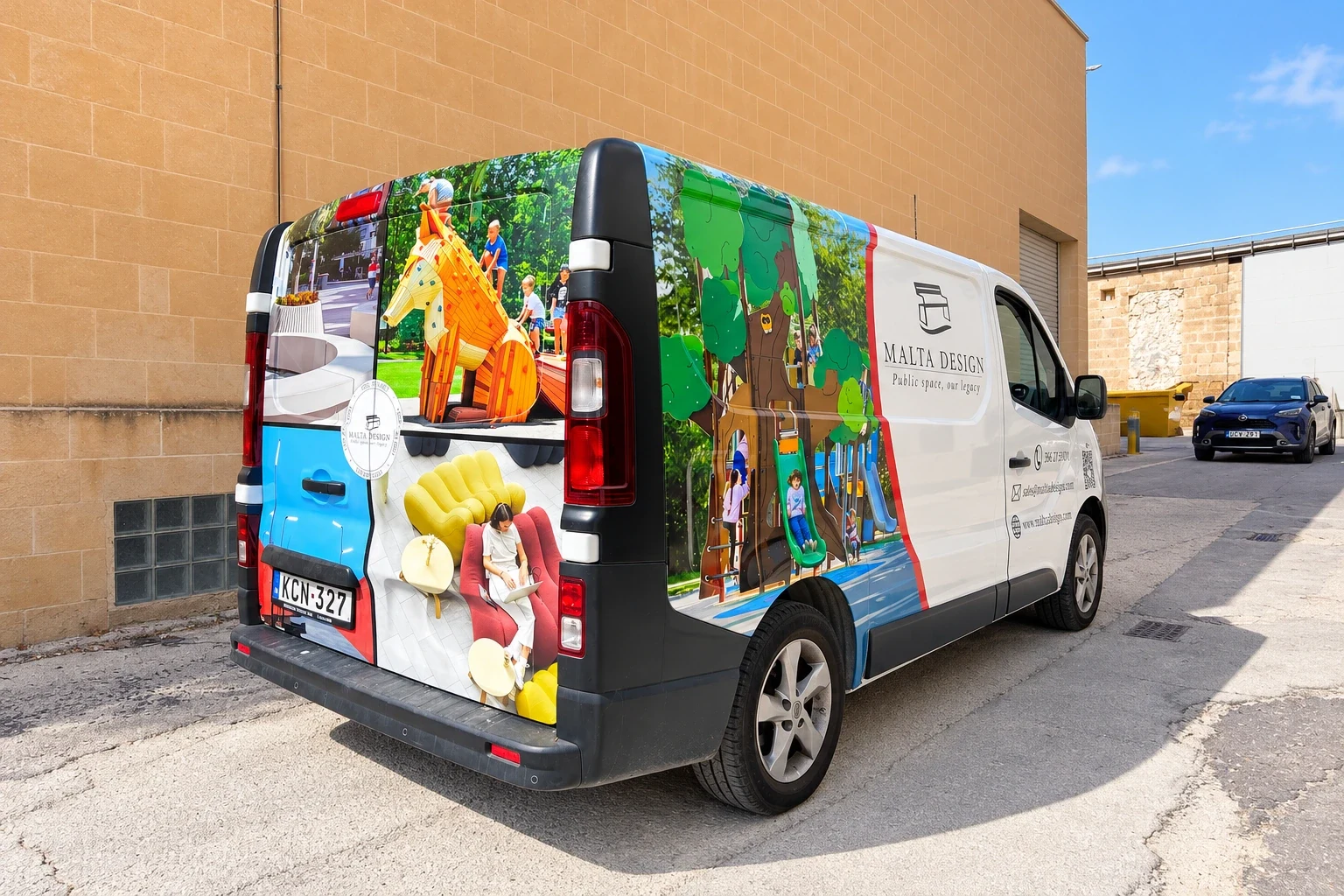White panel van wrapped in photographs of outdoor play equipment and interior furniture, parked beside a stone wall