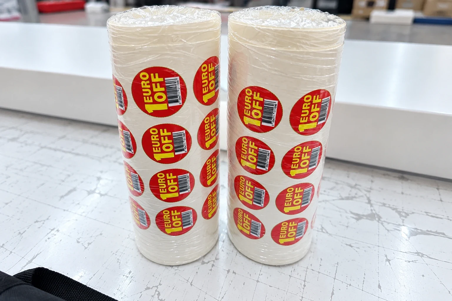 Two shrink-wrapped stacks of rolls of round red price-off labels on a workbench