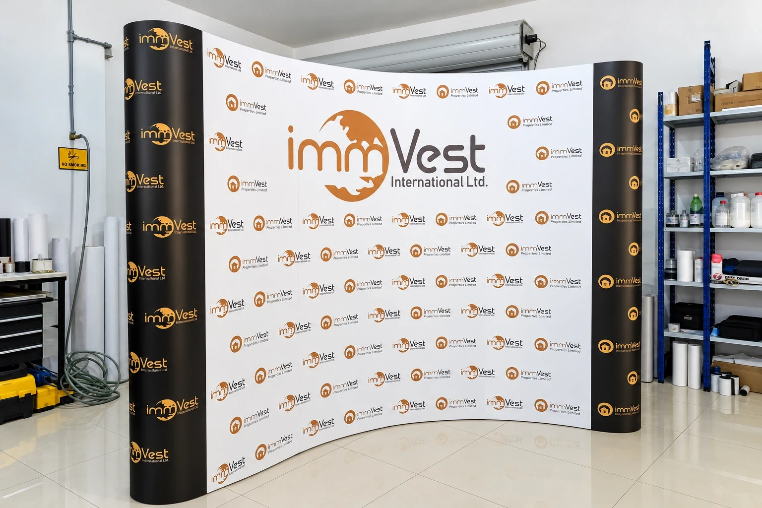 Curved fabric backdrop printed with a repeating property company logo, set up in a workshop