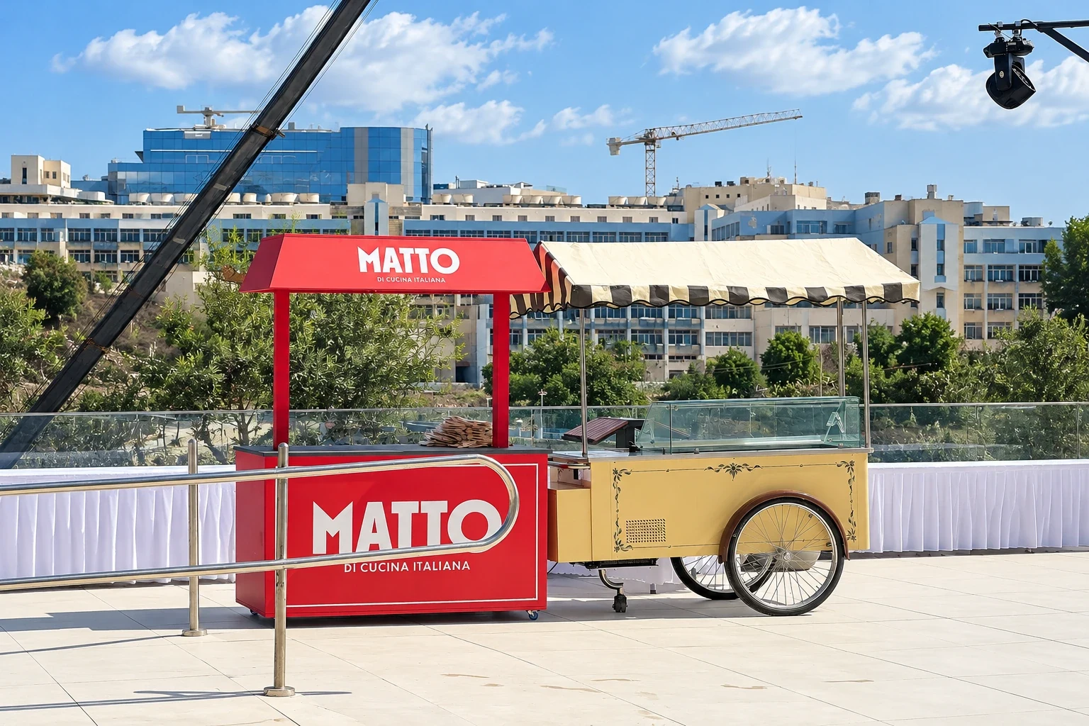 Red branded serving kiosk with a pitched canopy standing on a terrace beside a cream vintage cart