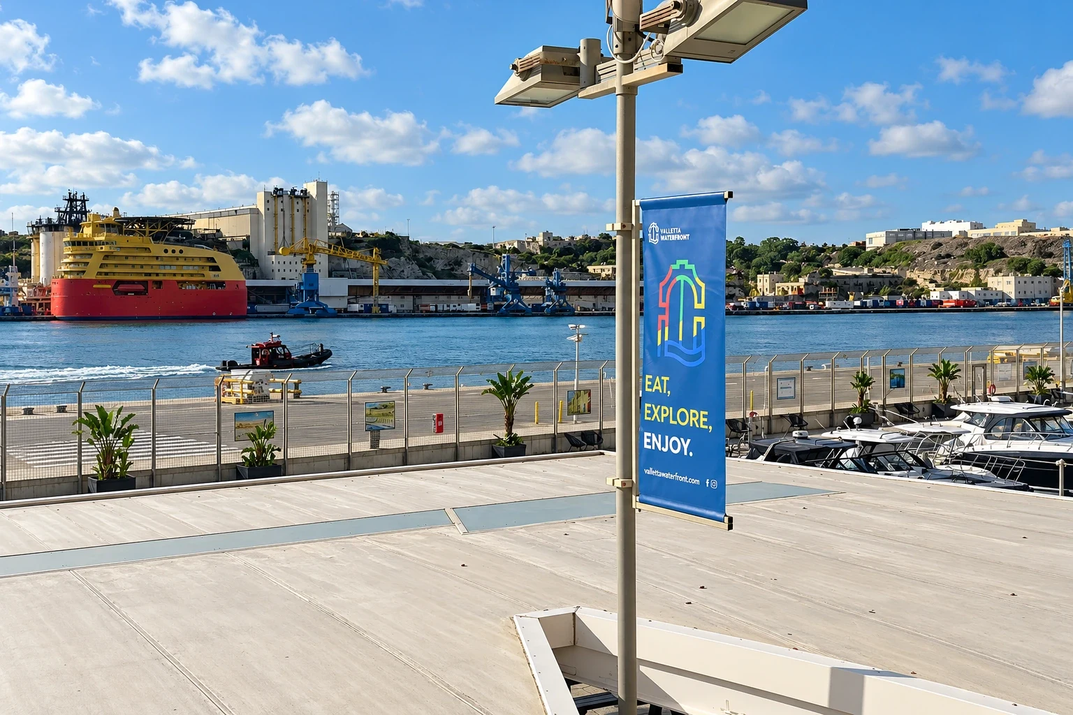 Blue lamp-post banner on a waterfront promenade with a harbour, moored ship and quay behind
